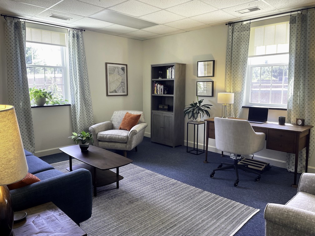 photo of therapy office, fabric chair, coffee table, desk, bookshelf, and plants